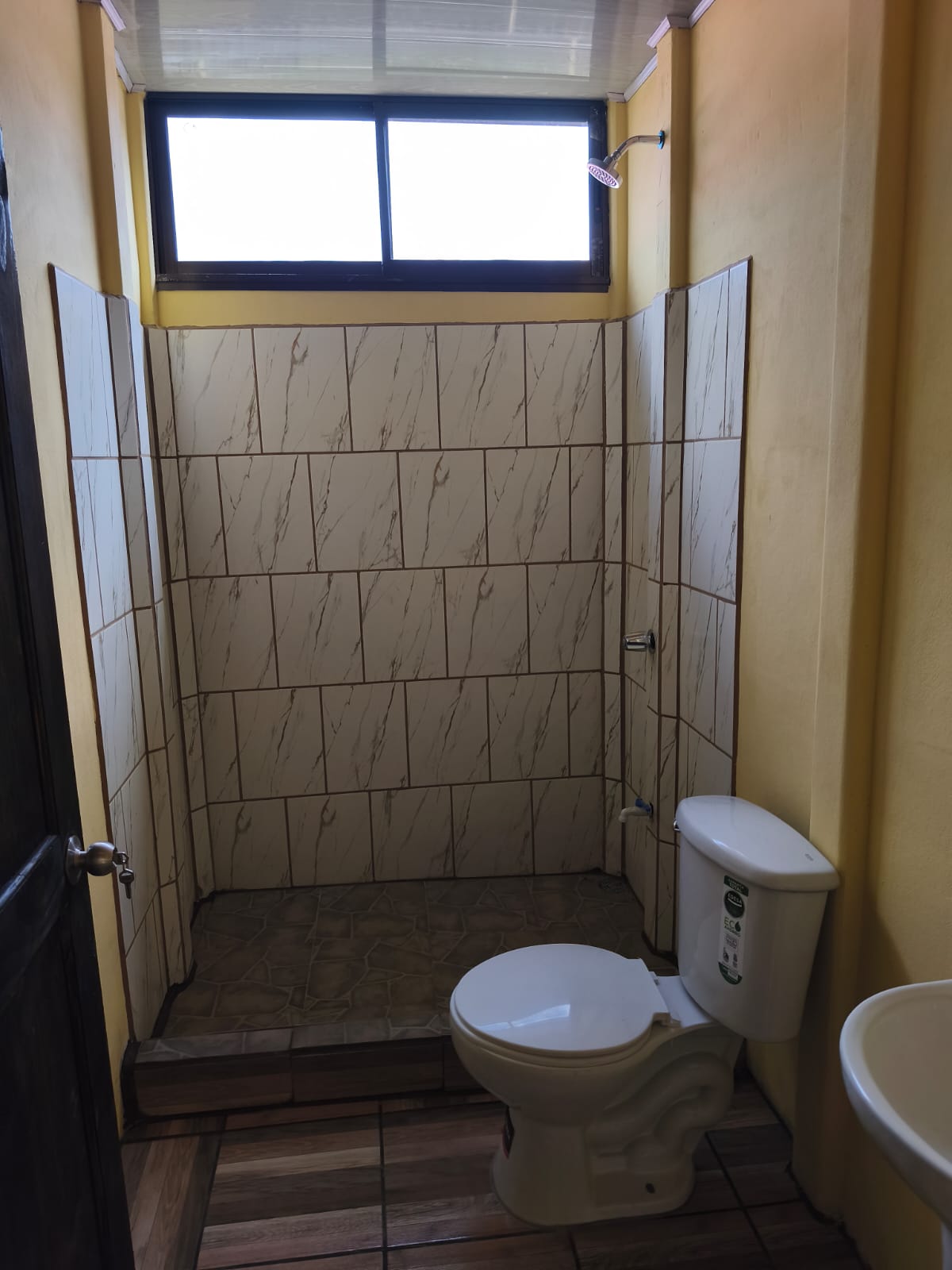 Baño interior con azulejos beige, ducha y sanitario blanco