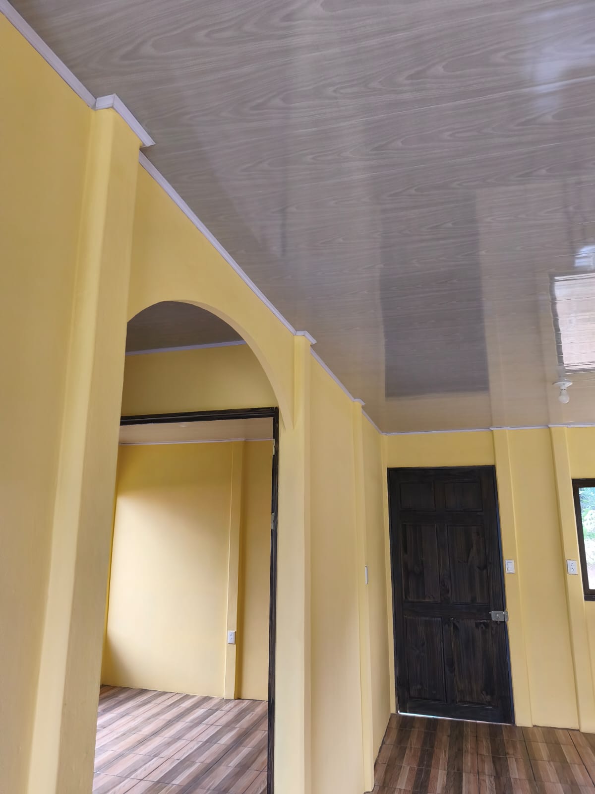 Interior de la casa con arco decorativo, cielo de PVC gris y pisos de porcelanato imitación madera